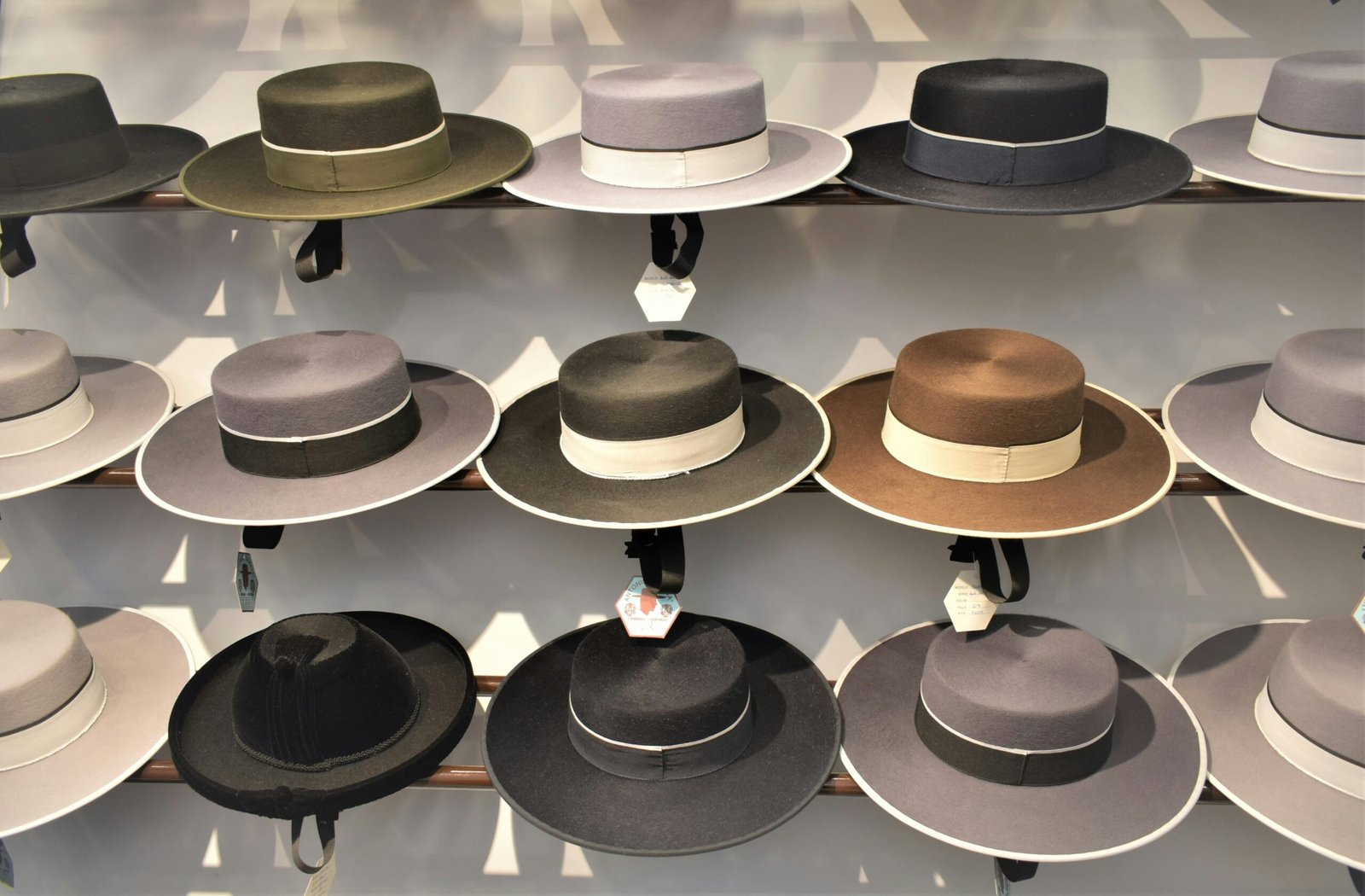 A close-up view of two wooden shelves filled with a variety of woven straw fedoras. The hats feature different weave patterns and colors, including cream, tan, and navy blue, with decorative bands in solid black, blue, or geometric patterns.